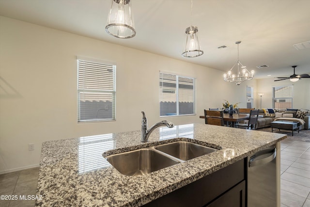 kitchen with light tile patterned flooring, sink, light stone counters, hanging light fixtures, and stainless steel dishwasher