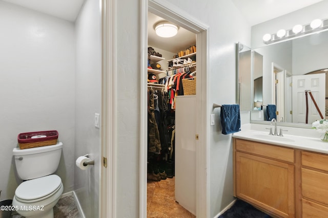 bathroom featuring toilet, a walk in closet, and vanity