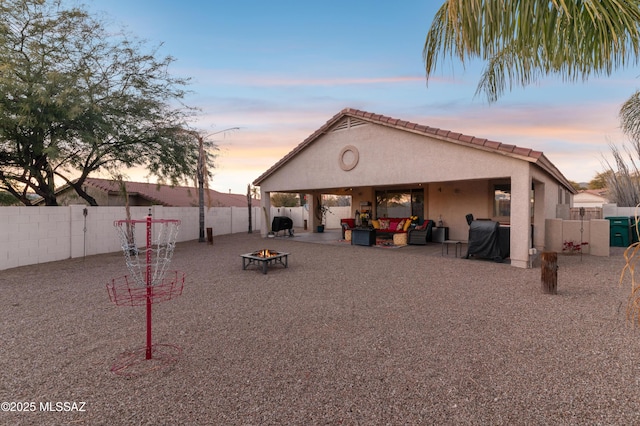 back of house at dusk featuring a tile roof, a patio area, a fenced backyard, an outdoor living space with a fire pit, and stucco siding
