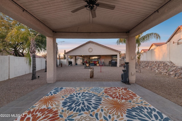 patio terrace at dusk with a ceiling fan and a fenced backyard