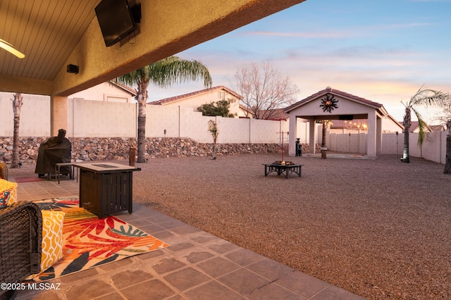 patio terrace at dusk with a fenced backyard, a fire pit, and a gazebo