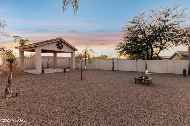 yard at dusk featuring a patio area, an outdoor fire pit, a fenced backyard, and a gazebo