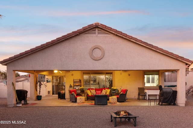 back of property at dusk with fence, an outdoor living space with a fire pit, a patio, and stucco siding