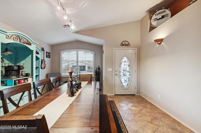 dining room featuring arched walkways, vaulted ceiling, and track lighting