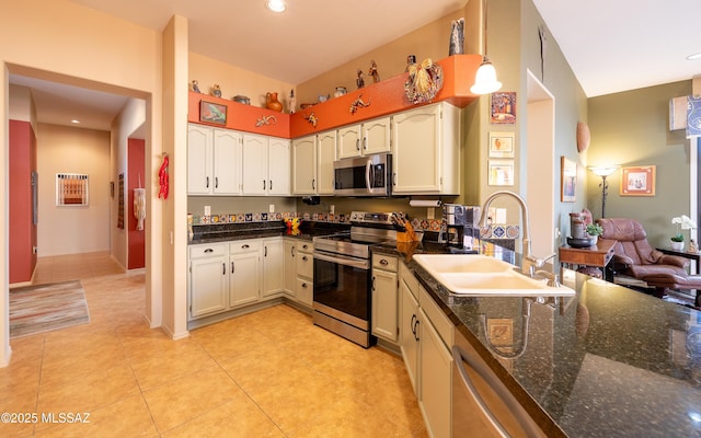 kitchen with dark stone counters, a sink, stainless steel appliances, light tile patterned flooring, and white cabinets