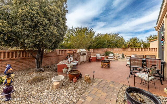 view of patio with a fenced backyard, an outdoor fire pit, an outdoor kitchen, and a grill