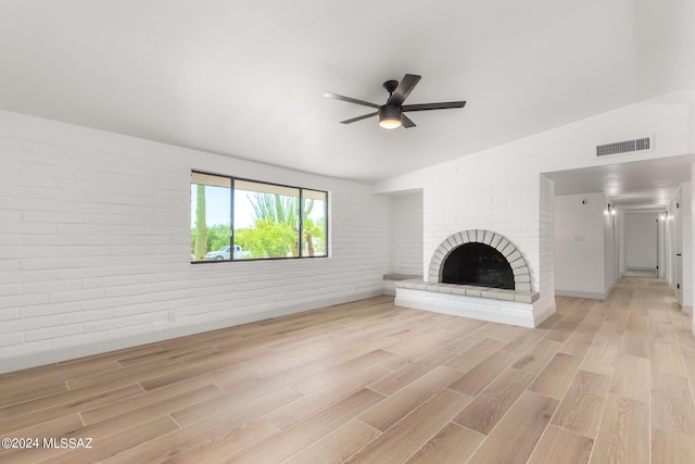 unfurnished living room featuring vaulted ceiling, brick wall, light hardwood / wood-style floors, and a brick fireplace