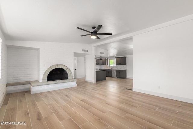 unfurnished living room with ceiling fan, lofted ceiling, a brick fireplace, and light wood-type flooring