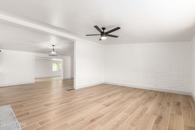 empty room featuring brick wall, ceiling fan with notable chandelier, and light wood-type flooring