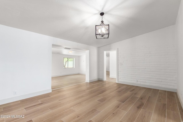 empty room featuring lofted ceiling, a notable chandelier, hardwood / wood-style flooring, and brick wall