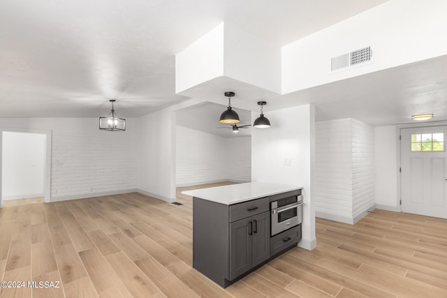 kitchen featuring stainless steel oven, brick wall, gray cabinets, and hanging light fixtures