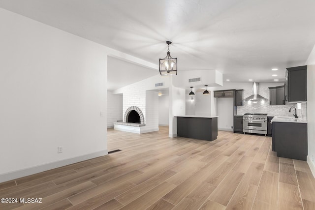 unfurnished living room with a fireplace, lofted ceiling, sink, a notable chandelier, and light hardwood / wood-style flooring