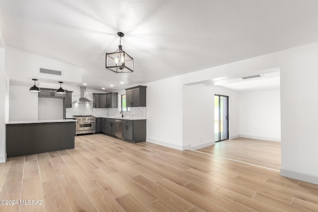 kitchen featuring pendant lighting, appliances with stainless steel finishes, backsplash, a notable chandelier, and wall chimney exhaust hood