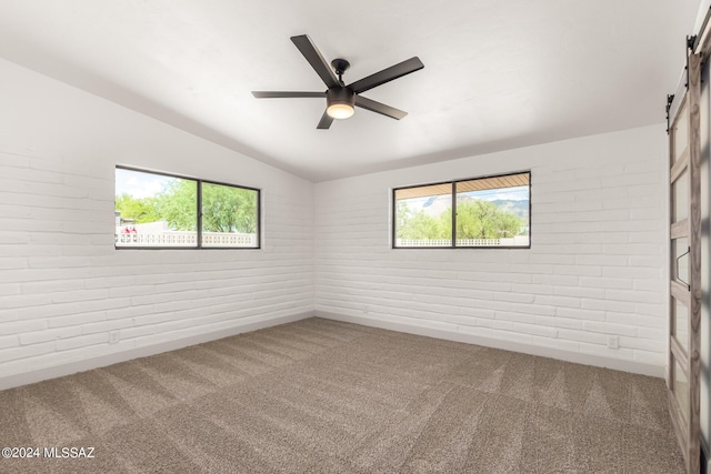 carpeted empty room featuring ceiling fan, brick wall, a barn door, and vaulted ceiling