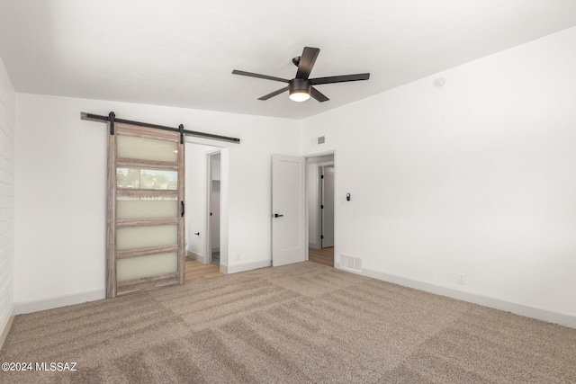 unfurnished bedroom with ceiling fan, a barn door, a walk in closet, light colored carpet, and a closet