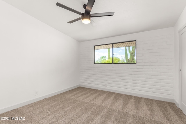 carpeted spare room featuring brick wall and ceiling fan