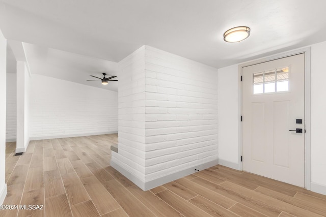 foyer entrance with ceiling fan, brick wall, and light wood-type flooring