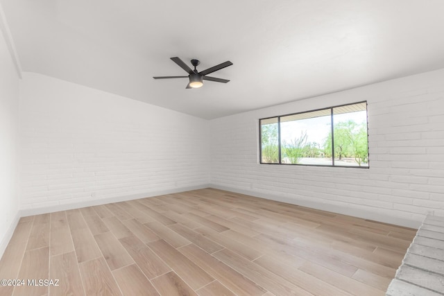 empty room with ceiling fan, brick wall, and light hardwood / wood-style floors