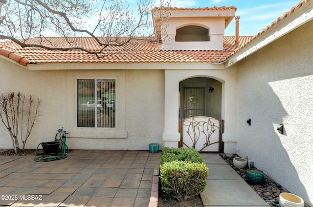 view of exterior entry with a tiled roof, a patio, and stucco siding