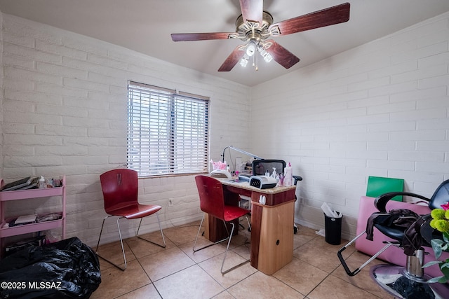 tiled office space featuring ceiling fan and brick wall