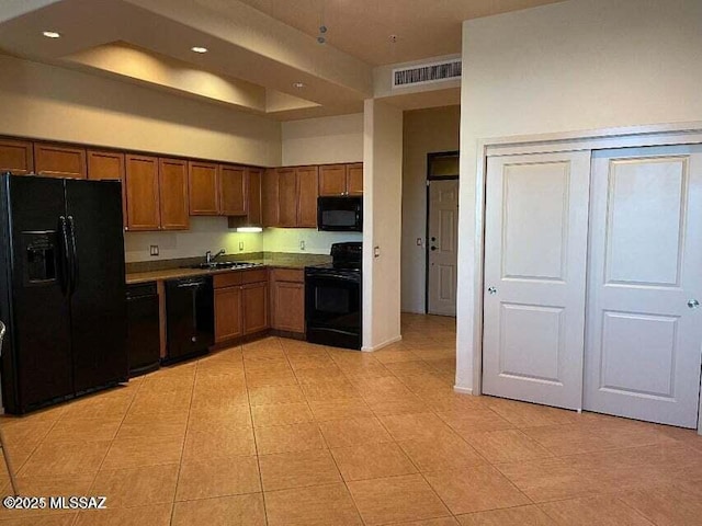 kitchen with sink, light tile patterned floors, black appliances, and a towering ceiling