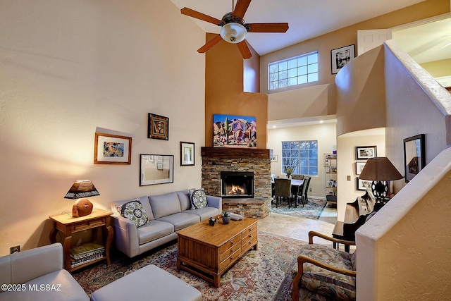 living room featuring a stone fireplace, ceiling fan, and a high ceiling