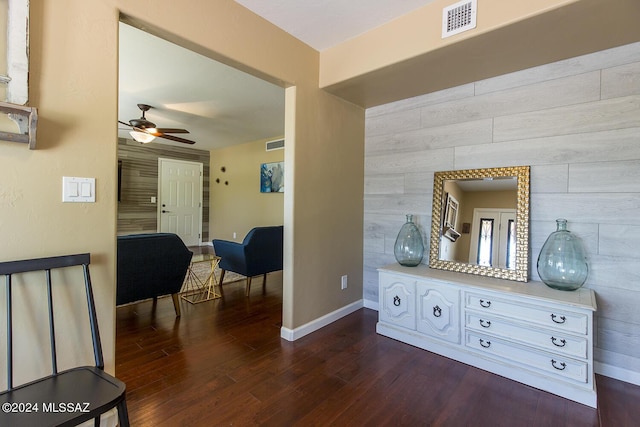 hallway with wooden walls, visible vents, baseboards, and dark wood-style flooring