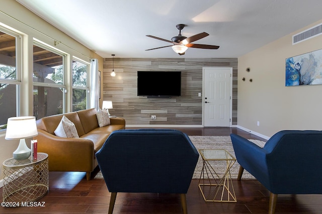 living room featuring dark hardwood / wood-style floors, ceiling fan, and wood walls