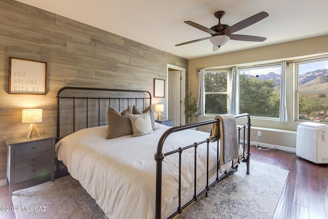 bedroom featuring a ceiling fan, hardwood / wood-style floors, wooden walls, a fireplace, and baseboards