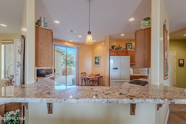 kitchen featuring pendant lighting, a breakfast bar area, white refrigerator with ice dispenser, and kitchen peninsula