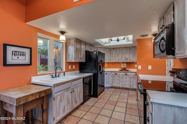 kitchen with light tile patterned flooring, sink, a textured ceiling, light brown cabinets, and black appliances