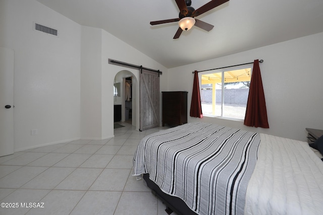 bedroom featuring ceiling fan, light tile patterned floors, a barn door, ensuite bath, and lofted ceiling