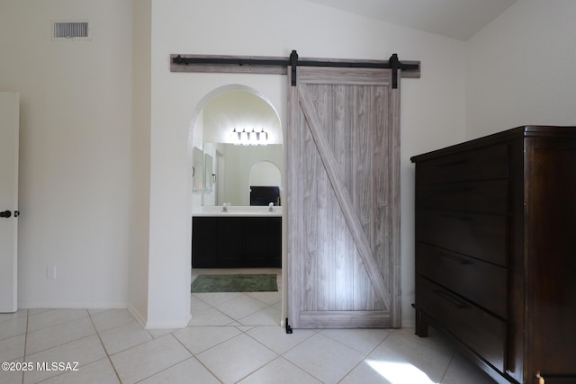 unfurnished bedroom featuring ensuite bathroom, sink, light tile patterned floors, a barn door, and lofted ceiling