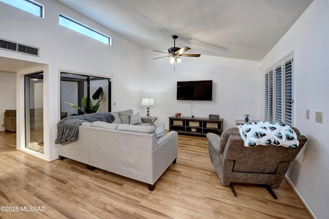 living room featuring ceiling fan, a towering ceiling, and light wood-type flooring