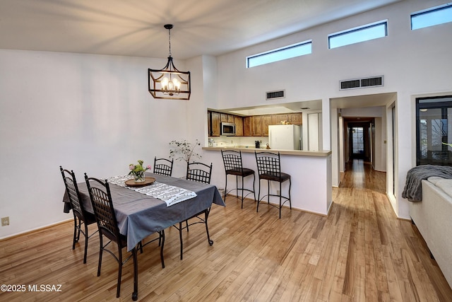 dining space featuring light hardwood / wood-style floors, a chandelier, and a high ceiling