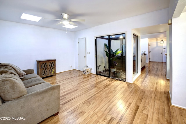 living room featuring a skylight, ceiling fan, and light hardwood / wood-style flooring