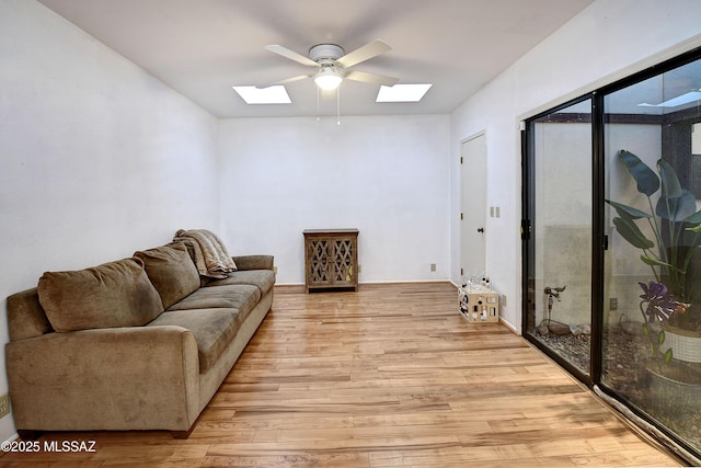 living room featuring ceiling fan, light hardwood / wood-style floors, and a skylight