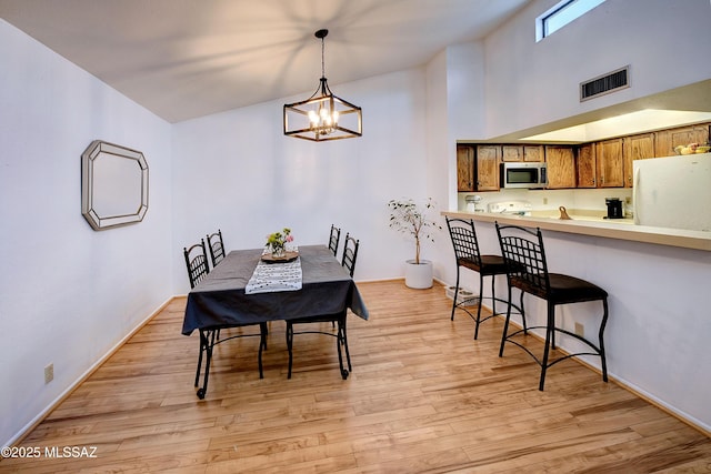 dining space with a towering ceiling, a chandelier, and light hardwood / wood-style flooring