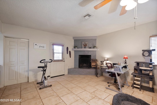 tiled home office with a brick fireplace, a textured ceiling, and ceiling fan