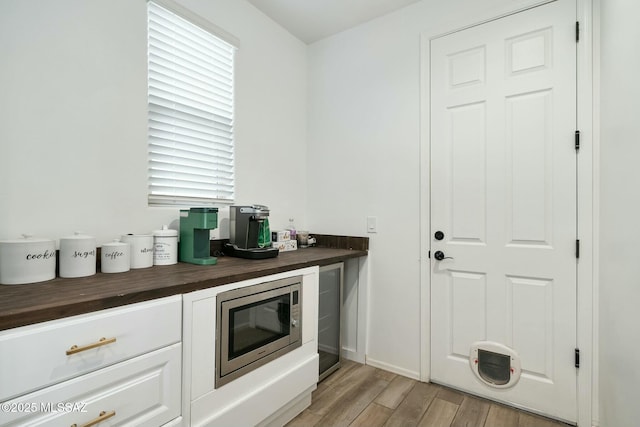 kitchen with stainless steel microwave, light hardwood / wood-style floors, white cabinetry, and butcher block counters