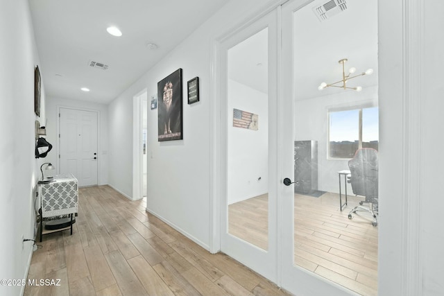 hall with light wood-type flooring, a notable chandelier, and french doors