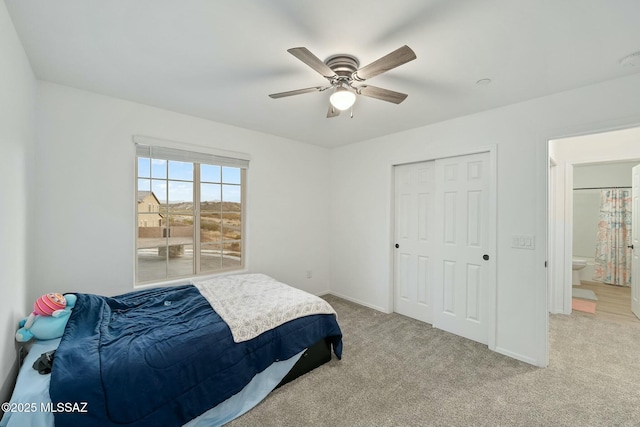 bedroom with a closet, ceiling fan, light colored carpet, and ensuite bath