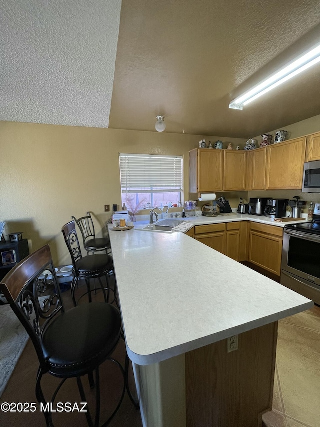 kitchen with kitchen peninsula, sink, a kitchen bar, a textured ceiling, and stainless steel appliances