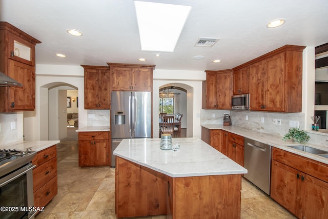 kitchen with visible vents, brown cabinetry, arched walkways, a kitchen island, and stainless steel appliances