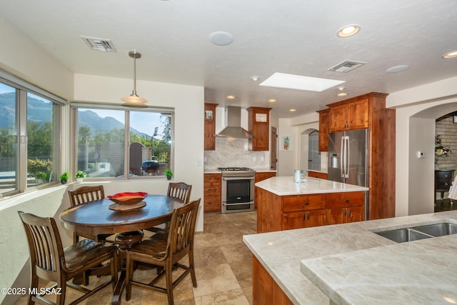 kitchen featuring wall chimney exhaust hood, visible vents, arched walkways, and stainless steel appliances