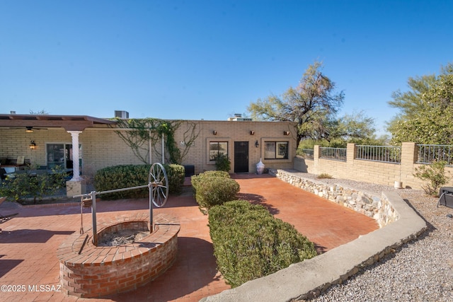 view of front of home featuring a patio area, an outdoor fire pit, fence, and brick siding