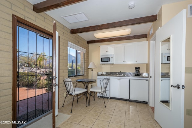 kitchen featuring visible vents, white microwave, beam ceiling, and white cabinetry