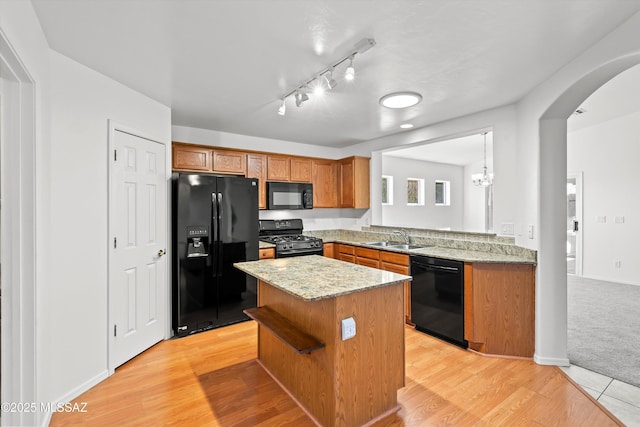 kitchen with black appliances, a kitchen island, decorative light fixtures, light hardwood / wood-style floors, and sink