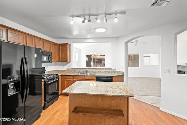 kitchen featuring black appliances, a center island, light stone countertops, light hardwood / wood-style floors, and sink