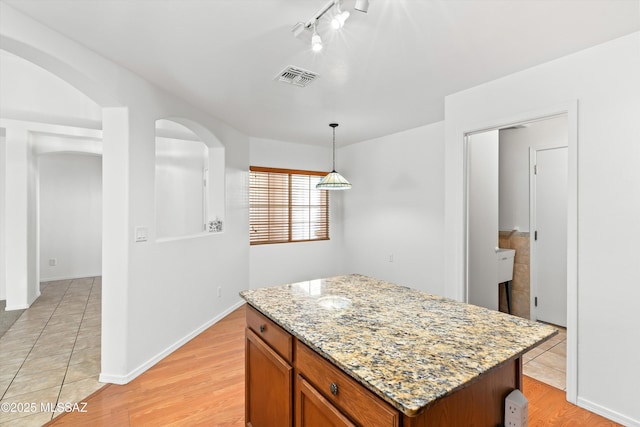 kitchen featuring light stone countertops, light wood-type flooring, a center island, and pendant lighting